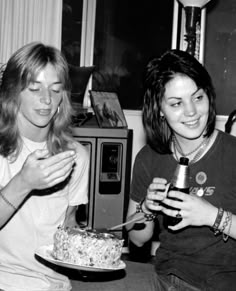 two women sitting next to each other with a cake on a plate in front of them