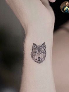 a small wolf tattoo on the left inner arm, with a woman's face in the background