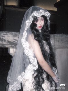 a woman in a wedding dress with long black hair wearing a veil and holding her hands behind her back