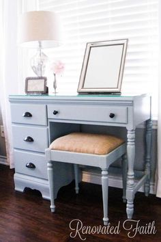 a desk with a mirror, stool and lamp on it