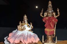 two statues sitting on top of a wooden table next to each other in front of a dark sky