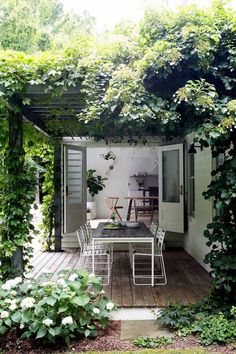 an outdoor dining area is surrounded by greenery and white chairs, along with a wooden deck