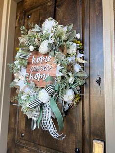 a wreath that says home sweet home on the front door with flowers and greenery