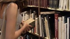 a woman reading a book in front of a bookshelf filled with many books