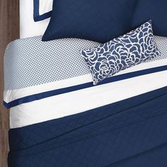 a bed with blue and white comforters and pillows on top of it, next to a wooden headboard