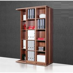 a wooden bookcase with many books and files on it's shelves in front of a gray wall