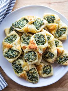 a white plate topped with spinach rolls on top of a wooden table next to a blue and white napkin