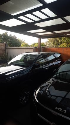 three cars parked in a carport with no doors on the top and one is black