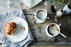 two cups of coffee and a piece of pie on a wooden table next to an open book