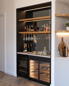 an empty bar with wine glasses and bottles on the shelves next to it, in front of a white wall