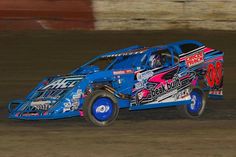 a blue truck with pink and white graphics on it's side driving around a track