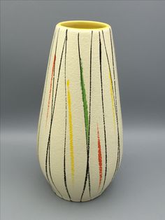 a white vase with multicolored lines painted on the outside and inside, in front of a gray background