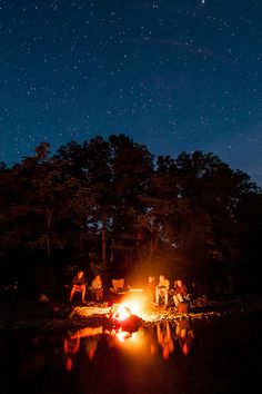 people sitting around a campfire at night with the stars in the sky above them