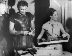 an old black and white photo of two people dressed in roman costumes, one holding a cake