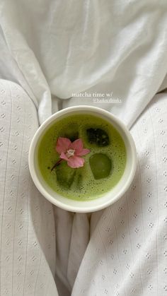 a white bowl filled with green liquid on top of a person's legs and holding a pink flower