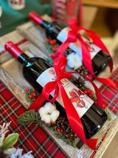 two bottles of wine sitting on top of a wooden tray covered in holly and pine cones