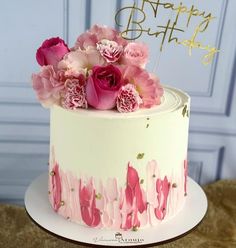 a birthday cake decorated with pink flowers and gold lettering on a white plate that says happy birthday