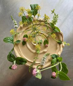 an arrangement of flowers and greenery on top of a metal surface, with the center surrounded by green leaves