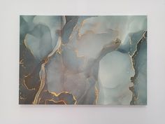 an abstract painting with gold and blue colors on white paper, hanging on a wall