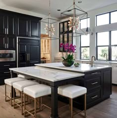 a kitchen with black cabinets and white marble counter tops, an island table surrounded by stools