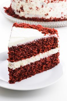 a slice of red velvet cake with white frosting on a plate next to the rest of the cake