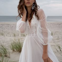 a woman standing on top of a beach next to the ocean wearing a white dress