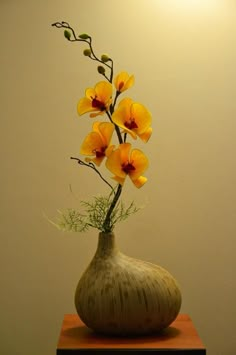 a vase filled with yellow flowers sitting on top of a wooden table next to a wall