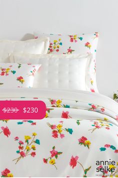 a white bed with pink and yellow flowers on it's comforter, next to a plant