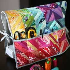 a colorful quilted bag with scissors, thread and spools on the table