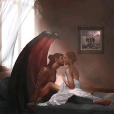 two women are kissing on a bed in a room with white drapes and paintings