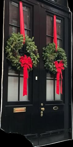 two christmas wreaths on the front door of a black building with red ribbons and bows