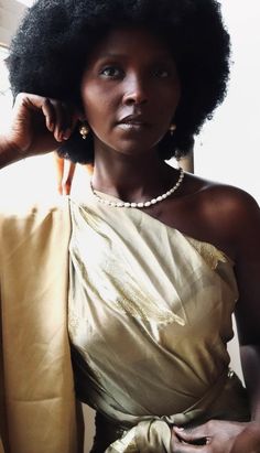 a woman with an afro wearing a gold dress and pearls on her head, posing for the camera