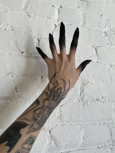 a person's arm with black and white tattoos on it, next to a brick wall