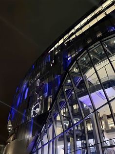 an illuminated building at night with blue lights on the glass and steel facade, along with other buildings in the background