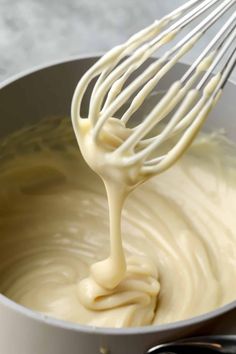 a whisk is being stirred in a saucepan with white batter on the side