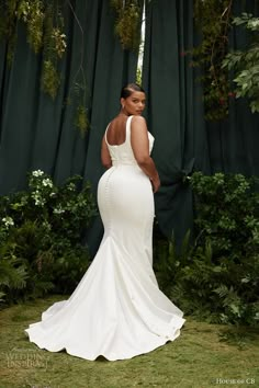 a woman in a white dress standing next to a green curtain with greenery on it