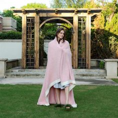 a woman standing in the grass wearing a pink blanket