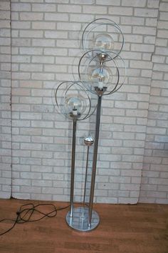 a metal and glass floor lamp in front of a brick wall with three lights on it