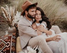 a man and woman sitting next to each other in front of tall grass with flowers