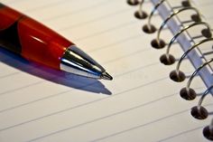 a red pen sitting on top of a notepad next to a spiral notebook with lined paper