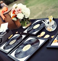 the table is set up for an event with cd's and flowers in vases