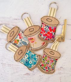 four sewing thread spools with flowers on them are hanging from keychains