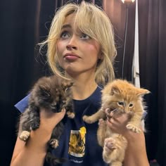 a woman holding three kittens in her hands and looking off into the distance with an intense look on her face