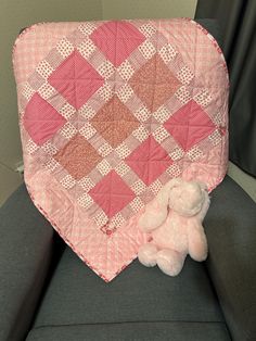 a pink teddy bear sitting on top of a couch next to a quilted blanket