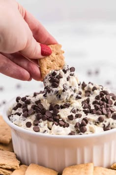 a hand dipping a cracker into a bowl filled with ice cream and chocolate chips