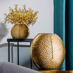 two gold vases sitting on top of a table next to a window with blue drapes