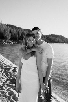 a man and woman standing next to each other on a beach near the water's edge