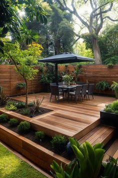 a wooden deck surrounded by plants and trees with an umbrella over the table in the middle