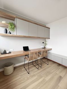 a desk with two chairs and a laptop on it in front of a wall mounted shelf