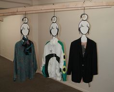 three mannequins are hanging on the wall in front of two coats and one jacket